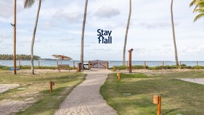 A pathway leading to a beach area with palm trees, a wooden gate, and a bench. - Rustic bungalow-beachfront condominium-017 (Tamandaré)
