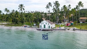 A white building with a green door, surrounded by palm trees and a beach. - Rustic bungalow-beachfront condominium-017 (Tamandaré)