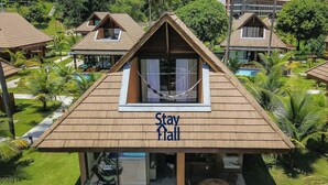 A Stay Hall with a triangular roof, a hammock, and a pool in the background. - Rustic bungalow-beachfront condominium-017 (Tamandaré)