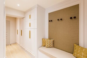 A hallway with a white wardrobe, a beige upholstered bench with cushions, and a textured wall with three circular decorations.