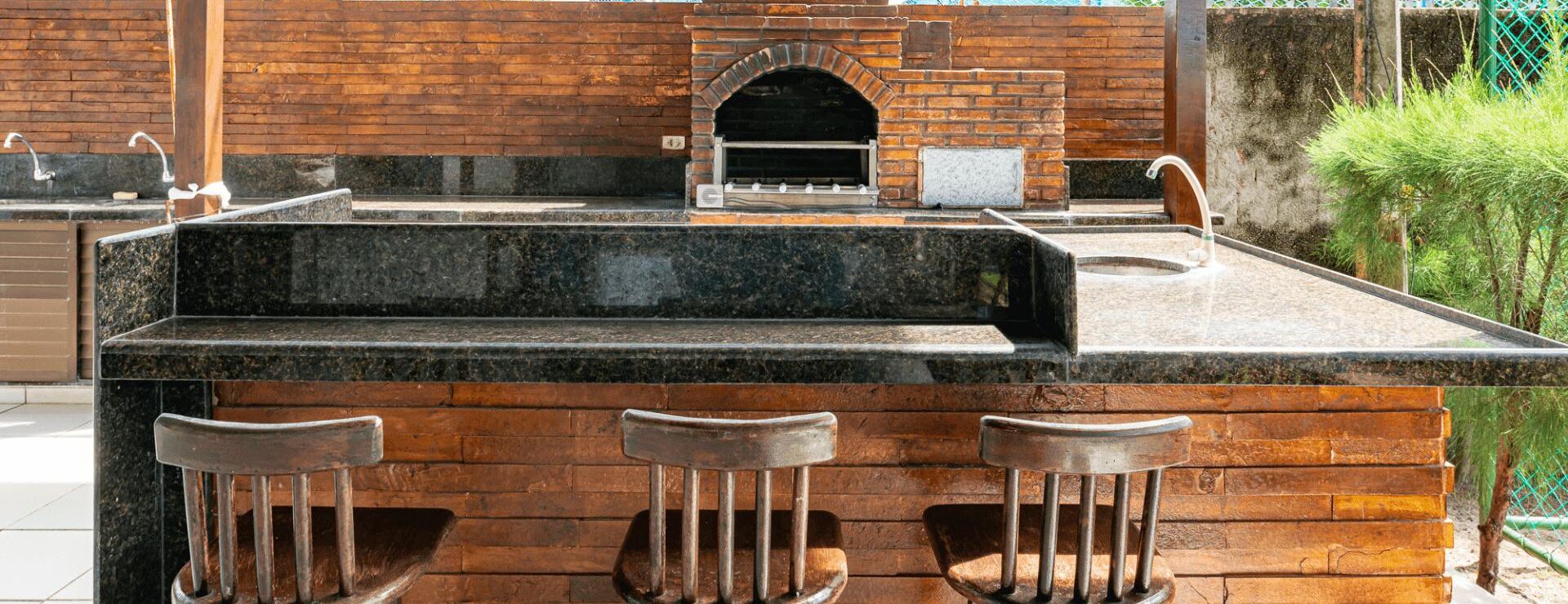A bar area with a brick oven, a granite countertop, and three stools.