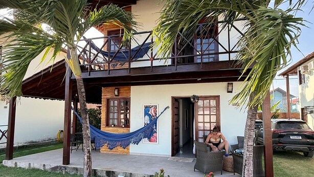 Una casa de dos pisos con un balcón, una hamaca y un jardín lleno de flores rojas.