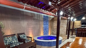 Una mesa de comedor de madera, un jacuzzi y una zona de estar con cojines estampados.