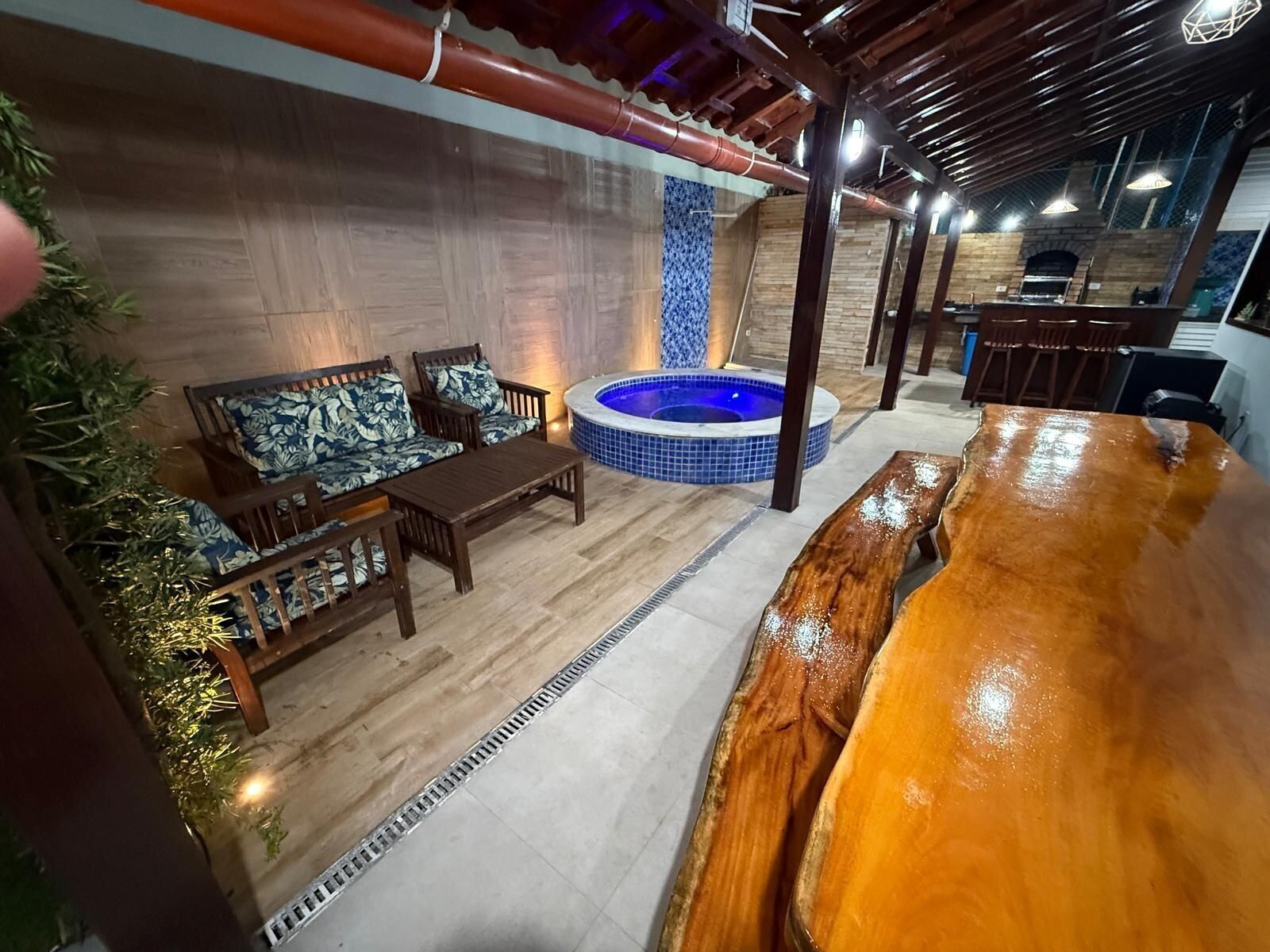 Un espacio interior acogedor con una mesa y sillas de madera, un jacuzzi y una pared de azulejos.