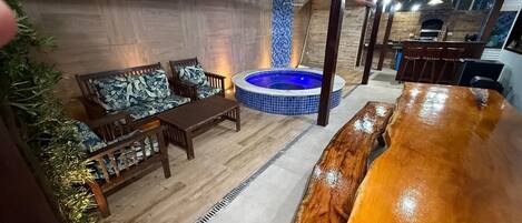 Un espacio interior acogedor con una mesa y sillas de madera, un jacuzzi y una pared de azulejos.