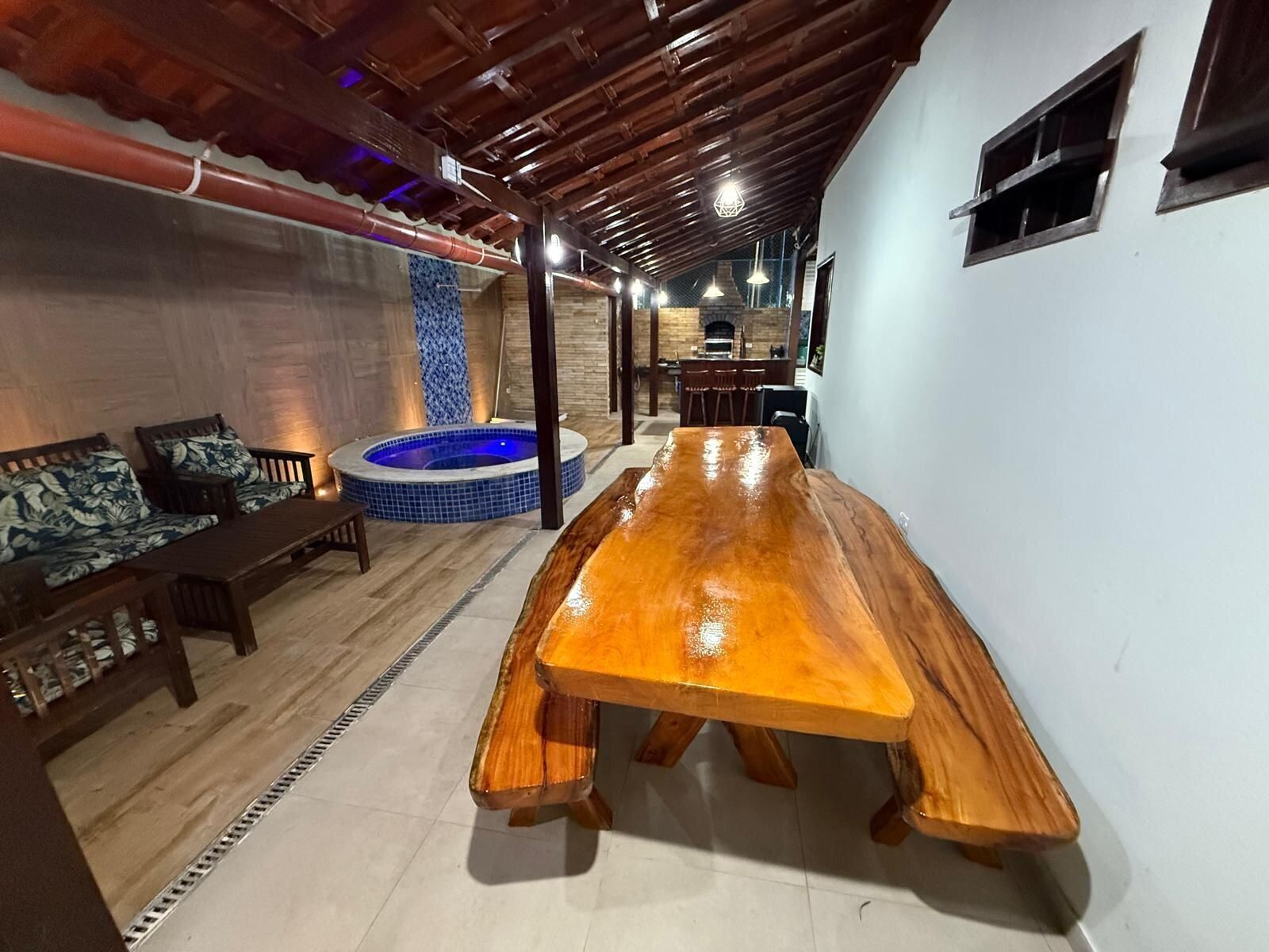 Un espacio interior amplio con una larga mesa de madera, una bañera de hidromasaje con azulejos azules y una zona de estar con muebles de madera.