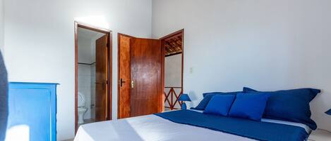 Un dormitorio con cama, un armario de madera, un baño visible a través de una puerta abierta y una lámpara azul.