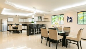 Une cuisine moderne avec des meubles blancs, un îlot central et un coin repas comprenant une table et des chaises en verre.