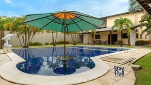 Une piscine avec un jacuzzi circulaire, entourée d’un patio aménagé avec des meubles d’extérieur et un parasol décoratif.