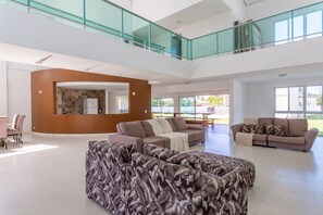 A spacious living area with a high ceiling, a glass railing balcony, and a view of the outdoors.