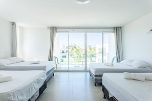 A hotel room with two beds, a balcony, and a view of buildings and greenery.