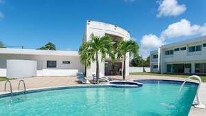 A swimming pool with lounge chairs and palm trees, surrounded by modern buildings. - Mansion with Private Pool and Jacuzzi 6 suites-082M (ipojuca)