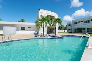 A swimming pool with lounge chairs and palm trees, surrounded by modern buildings.