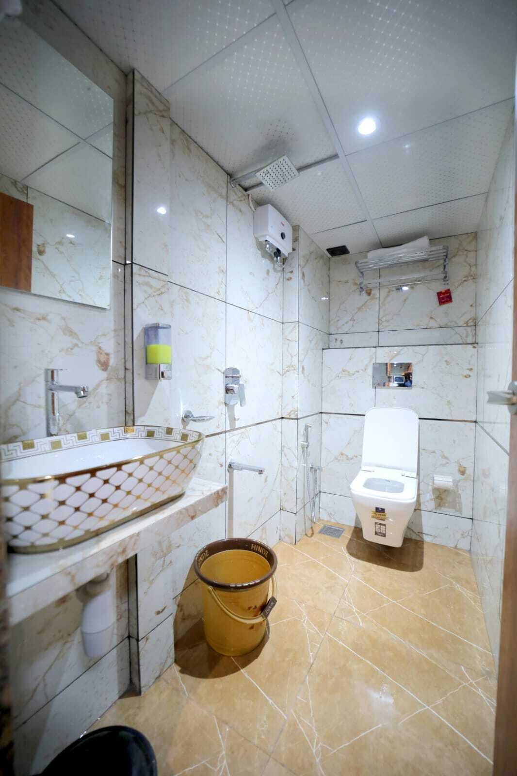 Un baño con lavamanos de mármol, inodoro, ducha y un cubo.