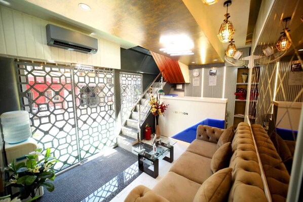 A modern hotel lobby with a reception desk, a staircase, a sofa, and decorative lighting. - N.M. Hotel (Mumbai)