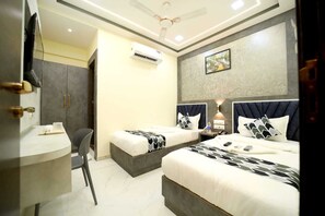 A hotel room with two beds, a desk, and a chair. There is an air conditioning unit on the wall and a painting above the beds. - N.M. Hotel (Mumbai)