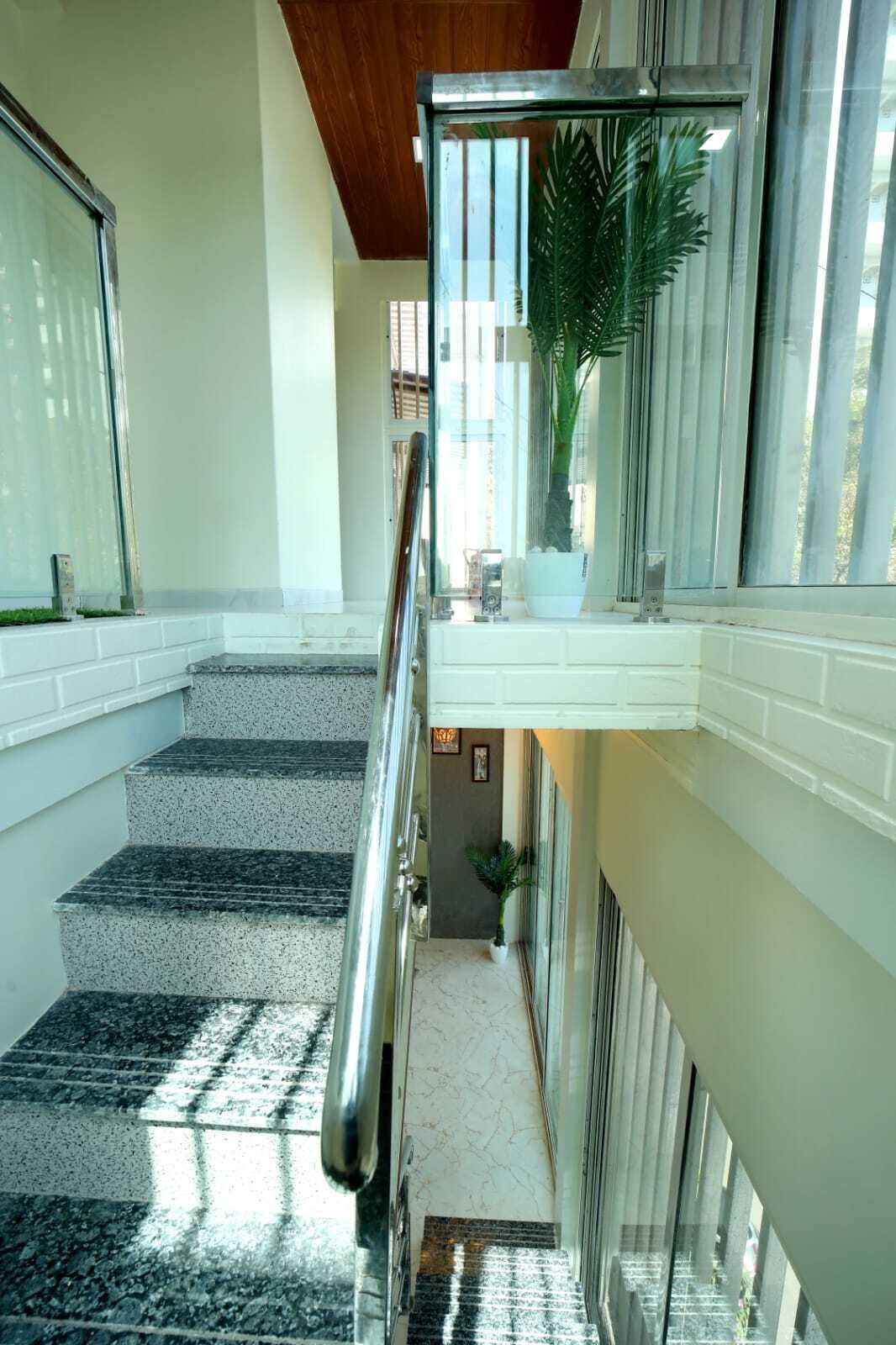Un escalier avec une rampe en verre, menant à un palier agrémenté d’une plante en pot et d’une petite table.