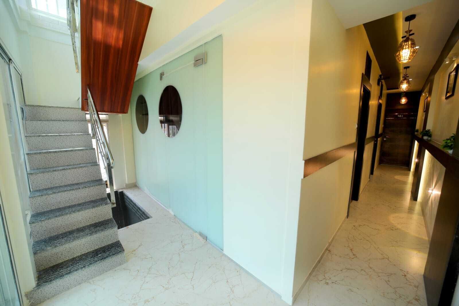 A hotel hallway with a marble floor, a wooden staircase, and a modern light fixture.