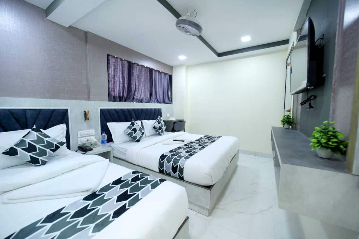 A hotel room with two beds, a ceiling fan, a TV, and a small balcony with plants.