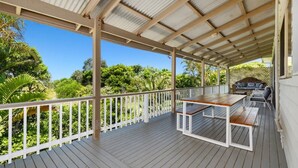 Eine überdachte Terrasse mit Tisch und Stühlen, umgeben von einem weißen Geländer und üppigem Grün.