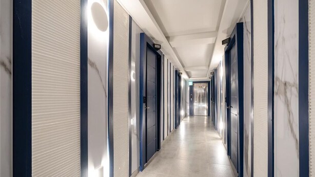 A long, narrow hotel corridor with closed doors on both sides, numbered signs above each door, and a light-colored floor. - Yeon Stay (Seoul)