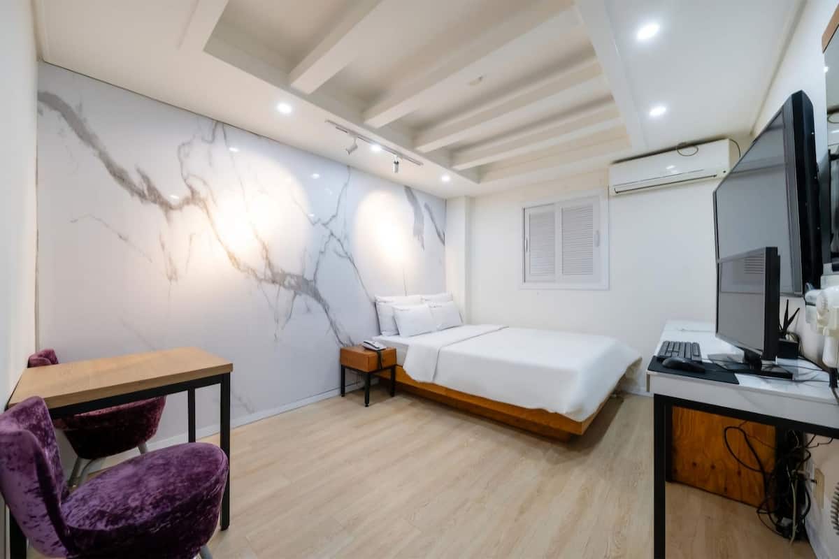 Un dormitorio moderno con cama, escritorio, silla y pared de mármol.