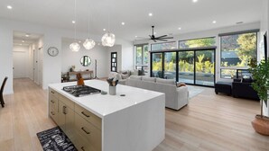 A modern kitchen with a central island, a dining area with a sofa, and a large sliding glass door leading to a balcony. - New Build Views hot tub and Deck (Sedona)