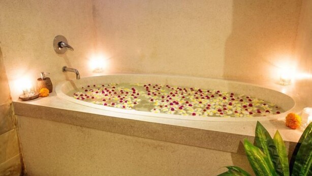 A bathtub filled with water and rose petals, with a flower arrangement on the side and a candle on the edge. - Ubud Luwih Nature Retreat (Bali)