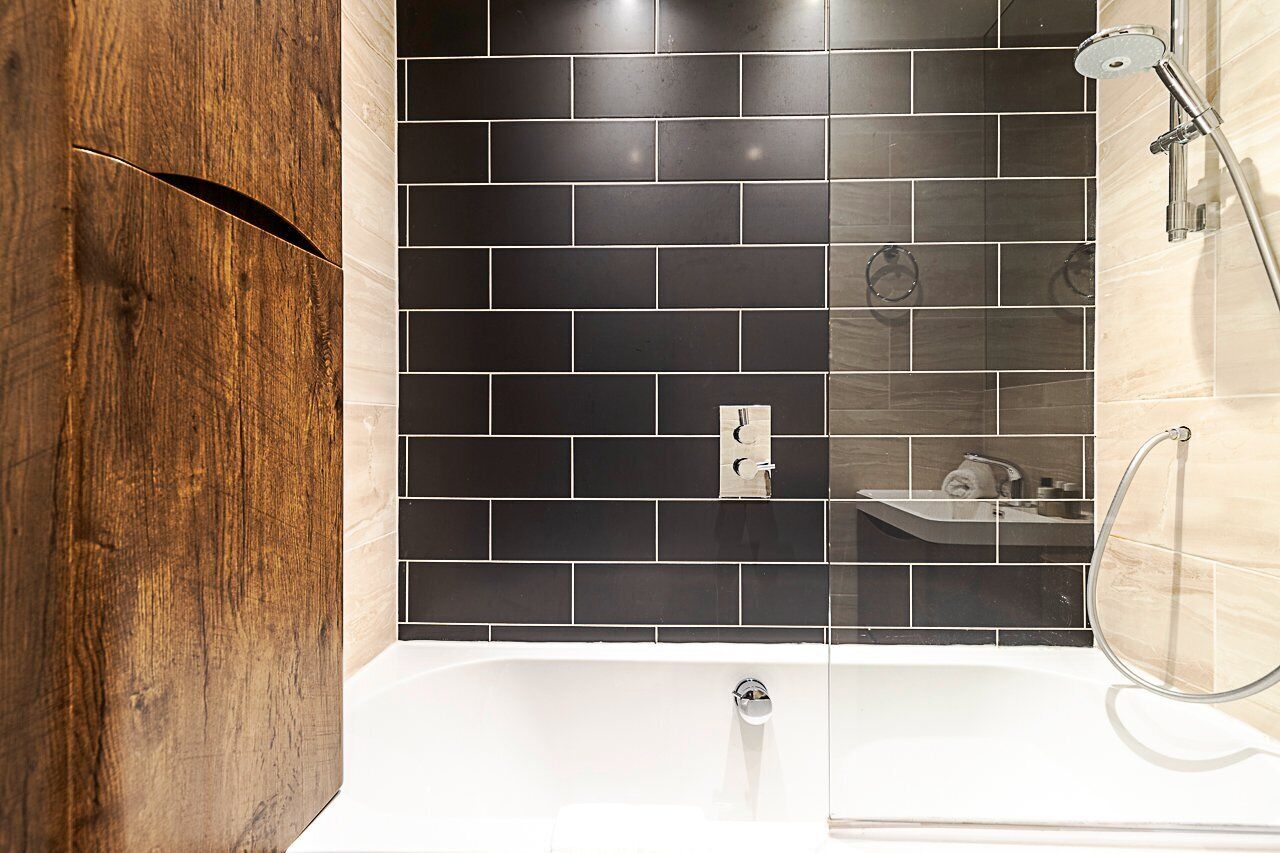 Une salle de bain moderne avec un mur d’accent en bois, une douche carrelée de noir et une baignoire blanche.