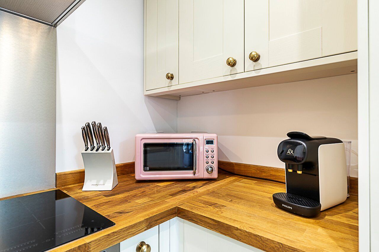 Une cuisine équipée d’un four à micro-ondes, d’une machine à café et d’un porte-couteaux, le tout posé sur un plan de travail en bois.