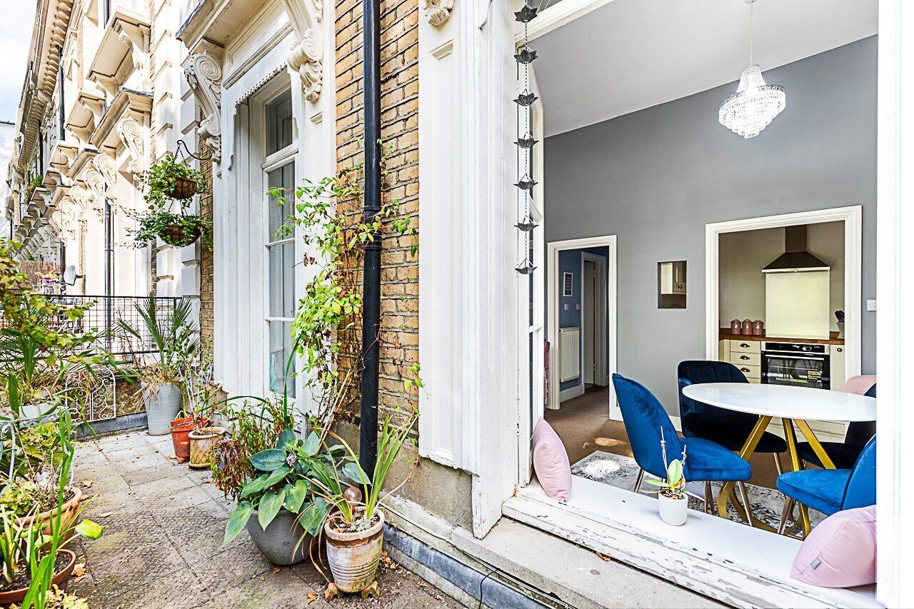 A cozy outdoor seating area with a table and chairs, surrounded by potted plants and a brick wall.
