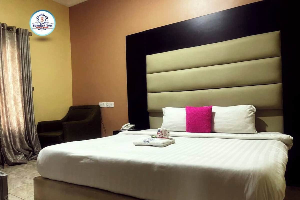 A hotel room with a large bed, a headboard, a chair, and a desk with a phone.