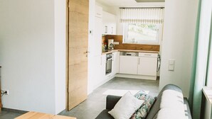 A modern living room with a sofa, a wooden coffee table, and a view into the kitchen. - Apartment Seeliebe (Oberried)
