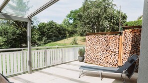 A balcony with a wooden fence, a lounge chair, and a stack of firewood. - Apartment Seeliebe (Oberried)