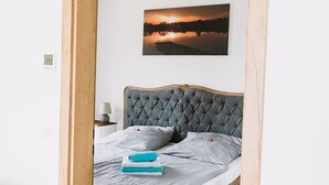 A bedroom with a wooden-framed bed, grey bedding, and a sunset painting on the wall. - Apartment Seeliebe (Oberried)