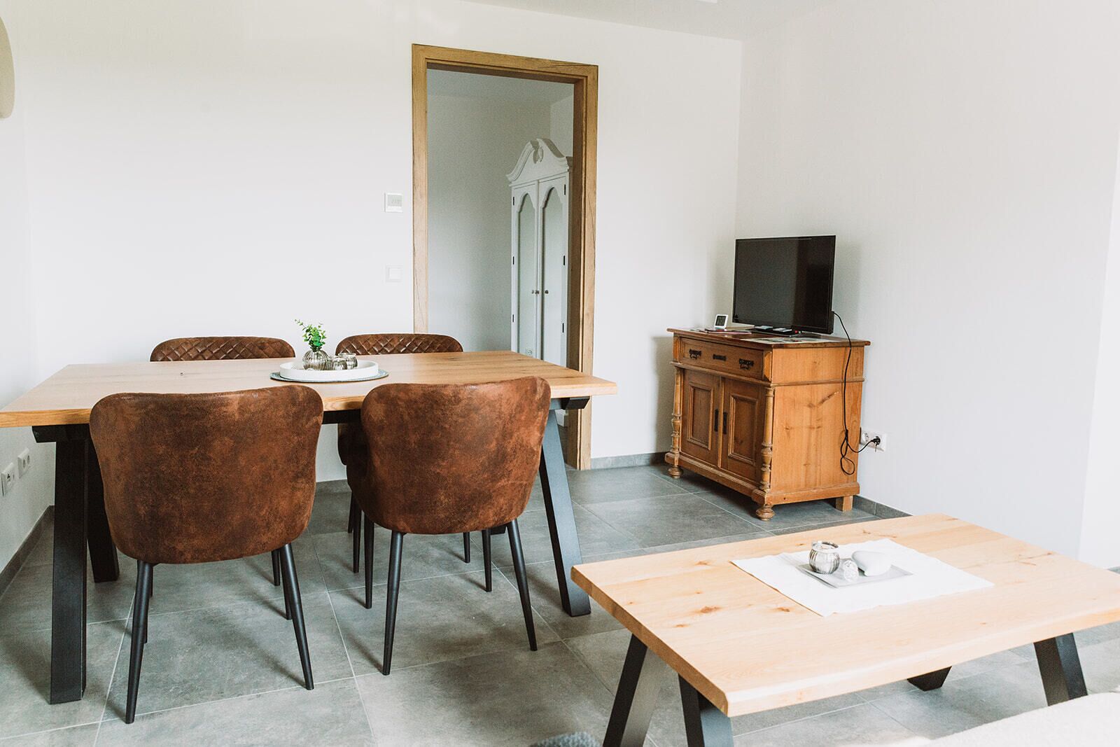Ein Essbereich mit Holztisch und -stühlen, einem Fernseher auf einer Holzkommode und einem Spiegel an der Wand.