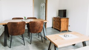 A dining area with a wooden table and chairs, a television on a wooden cabinet, and a mirror on the wall. - Apartment Seeliebe (Oberried)
