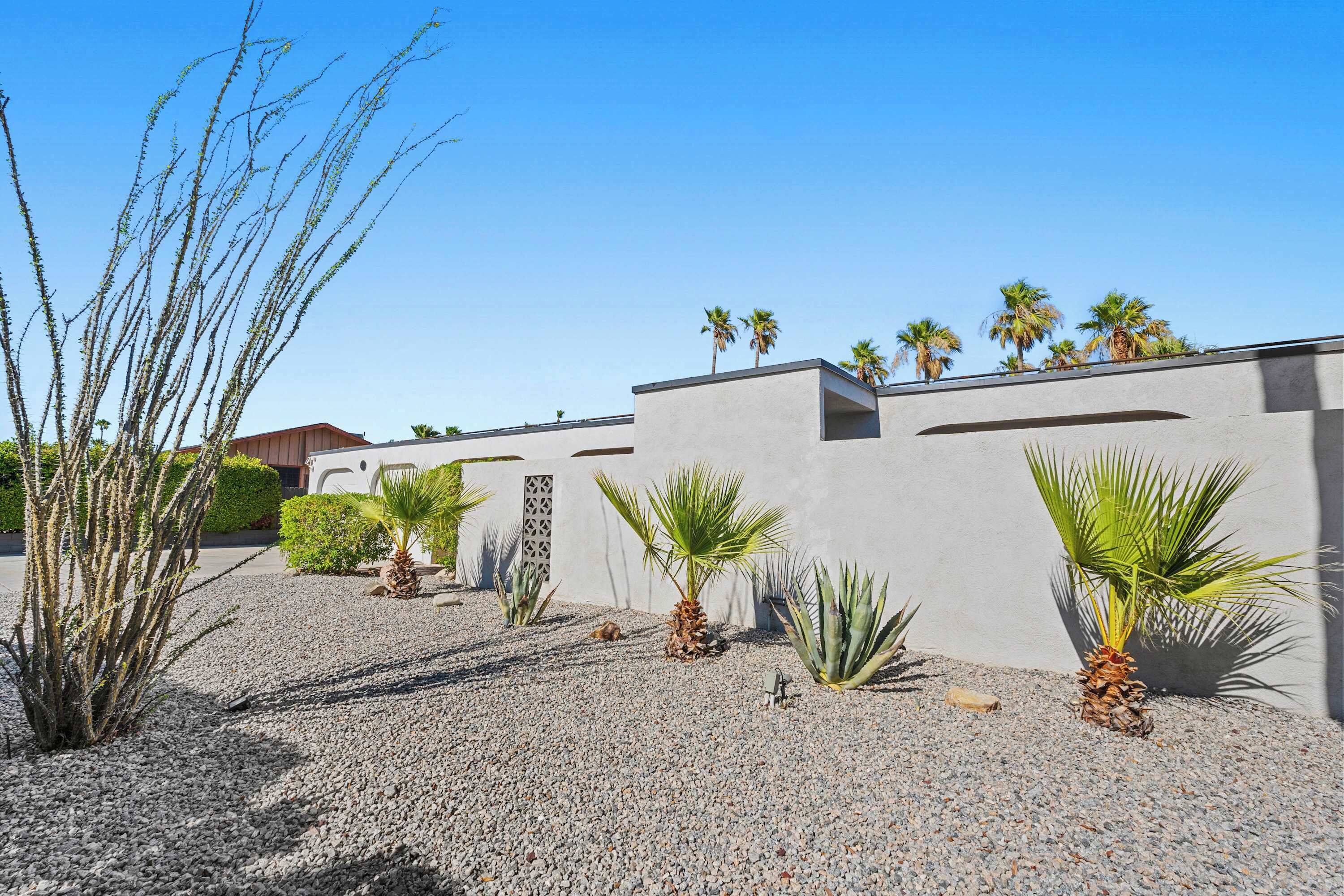 A modern building with a gravel courtyard, palm trees, and a clear blue sky.