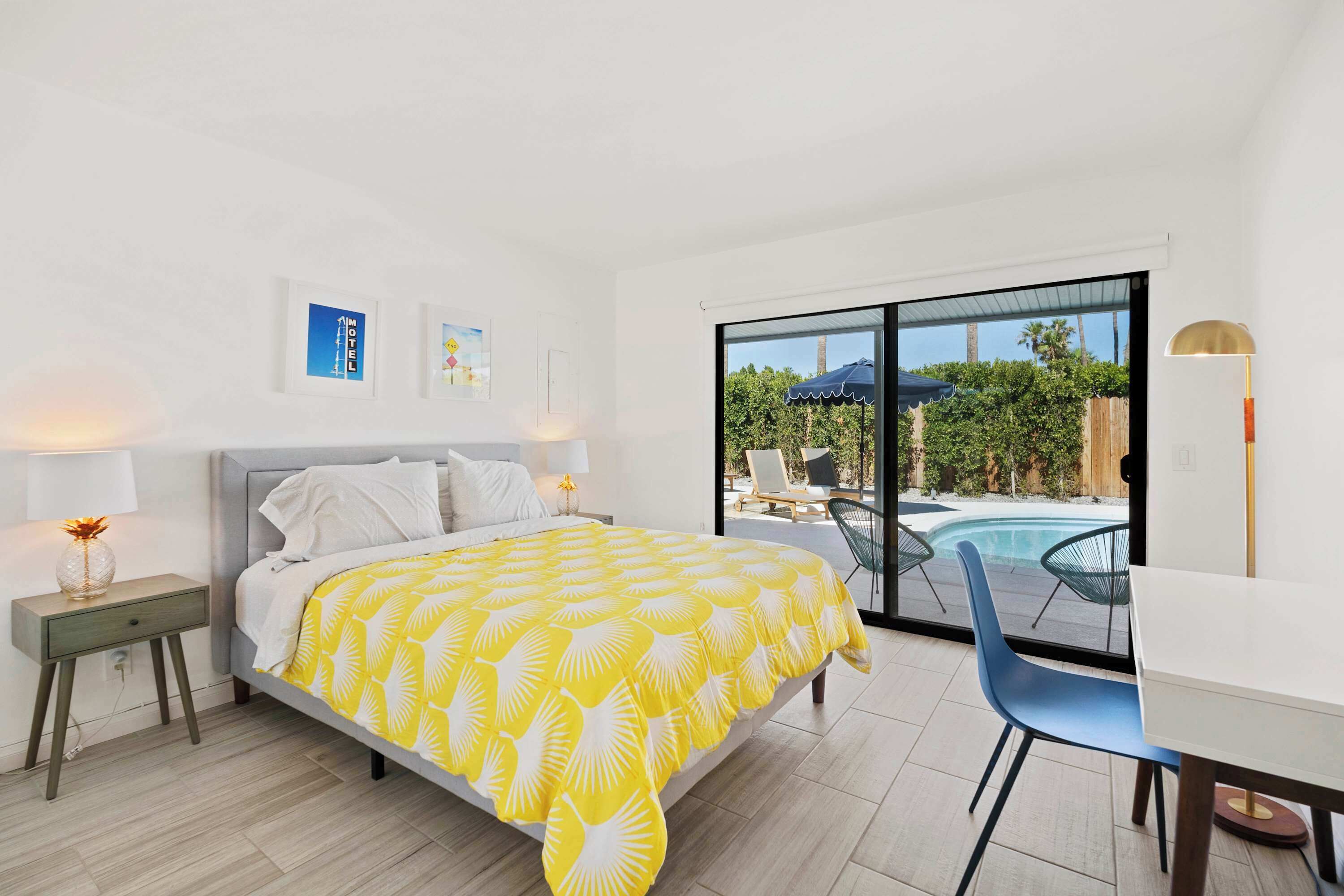 Una camera da letto con un letto, un comodino, una scrivania e una sedia. Si vede una finestra con vista su una piscina e del verde all'esterno.
