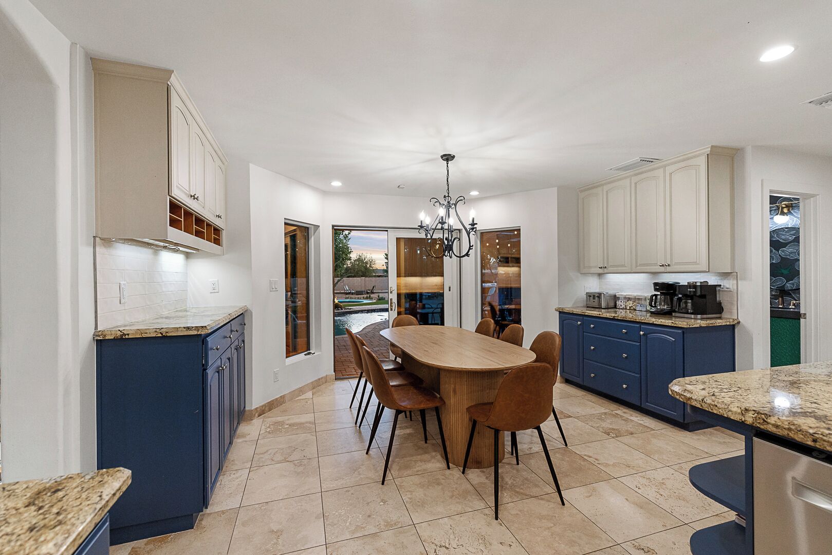 A modern kitchen with a dining area, featuring a large island, built-in cabinets, and a view of the backyard.