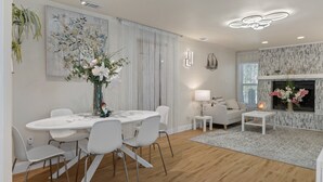 Un salon moderne avec un coin repas, comprenant une cheminée, des meubles blancs et des plantes décoratives.
