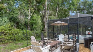Un espace extérieur aménagé avec des sièges, abrité par une structure, comprenant des fauteuils Adirondack, une table en bois et une paroi en verre.