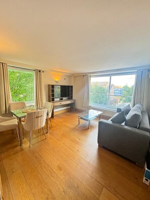 A modern living room with a glass coffee table, grey sofa, and a dining area with a glass table and chairs. - Westwood House (London)
