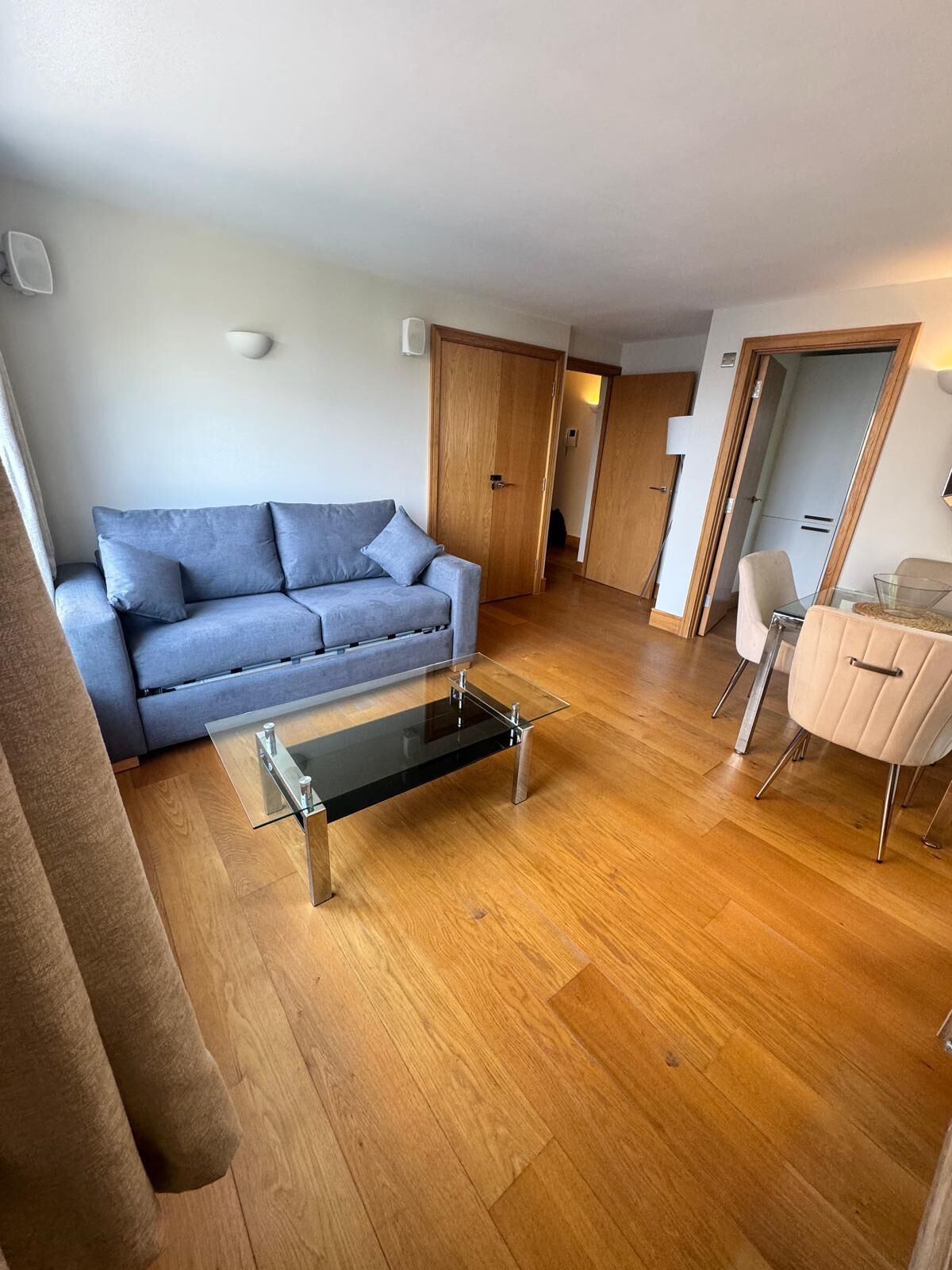 En moderne stue med en grå sofa, et glasbord og trægulv.