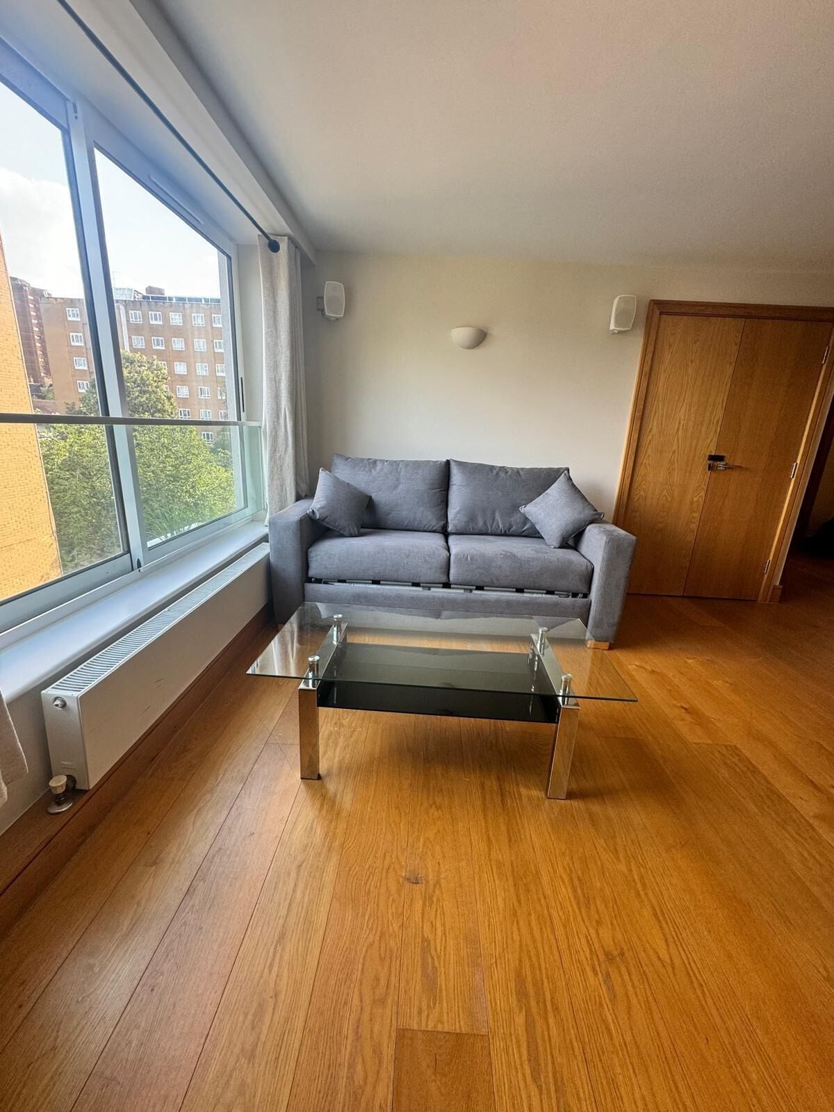 Una sala moderna con un sofá gris, una mesa de centro de cristal y suelo de madera.