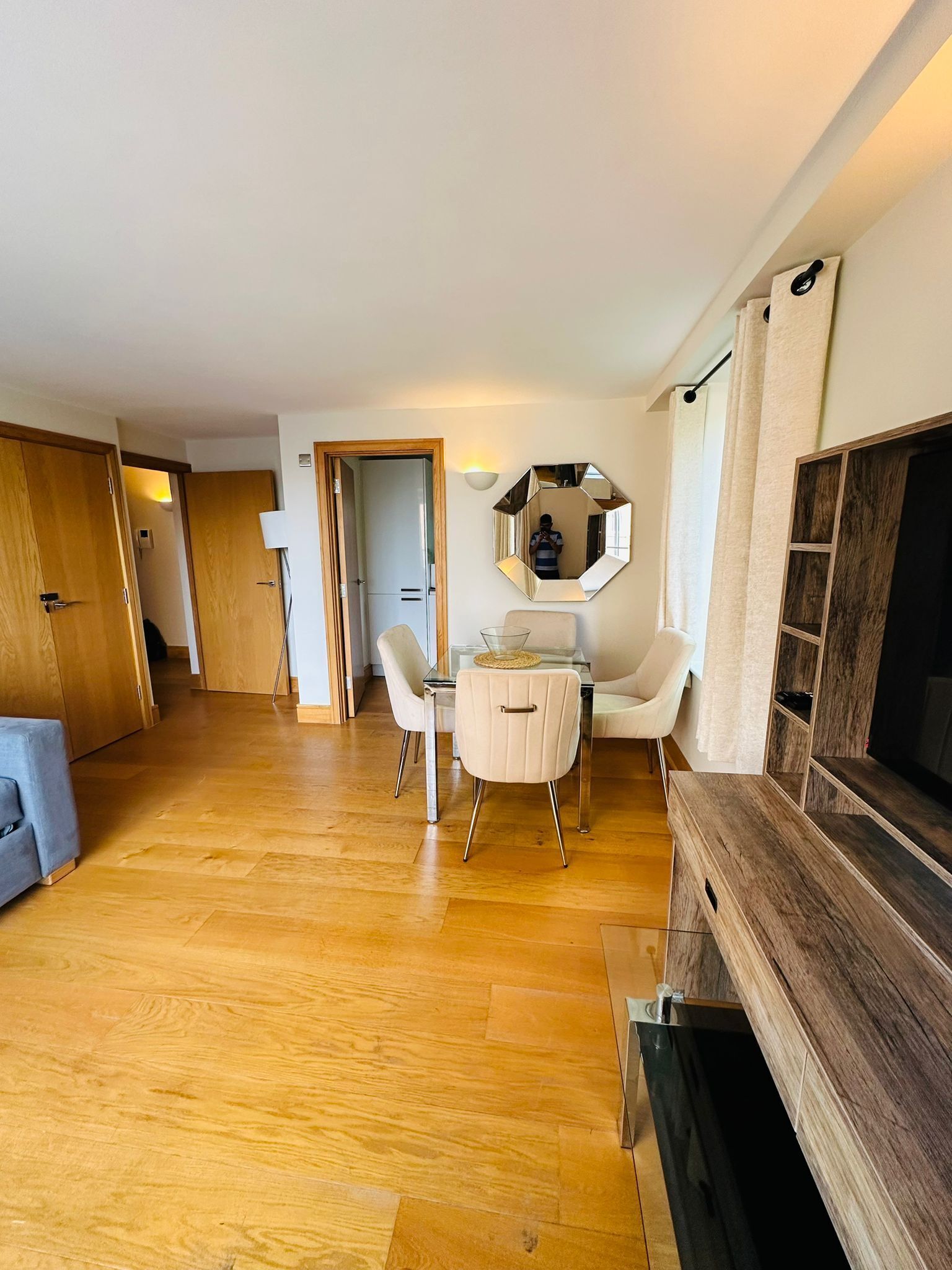 Ein geräumiger Wohnbereich mit Holzboden, einem Esstisch mit Stühlen, einer Couch, einem TV-Schrank und einem Spiegel.