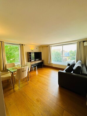 A living room with a wooden floor, a sofa, a TV stand, and a dining table with chairs. - Westwood House (London)