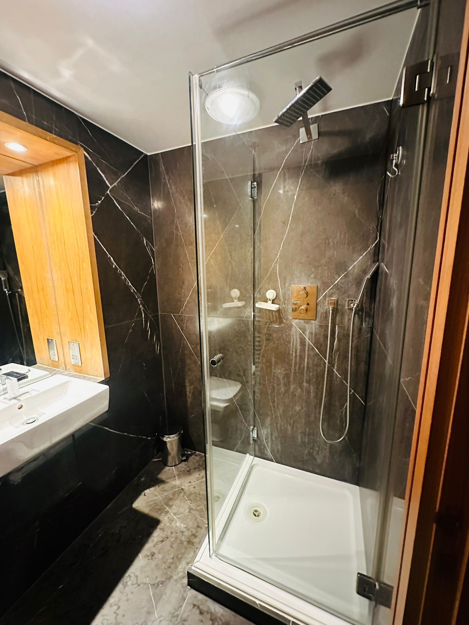A modern bathroom with a glass-enclosed shower, a white sink, and a marble-tiled wall.
