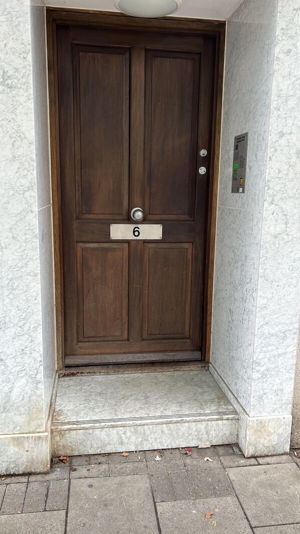 A dark wooden door with a number plate marked '6', a doorbell, and a keypad on the wall to the right. - Westwood House (London)