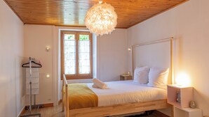 A bedroom with a wooden bed, a hanging light fixture, a window with curtains, a bedside table, and a shelf with a globe. - Rimaye Blanche - A bright and cozy 1 bed apartment. (Chamonix-Mont-Blanc)